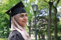 Naimal Chisti, wearing a hijab and a black graduation cap, smiles into the distance.
