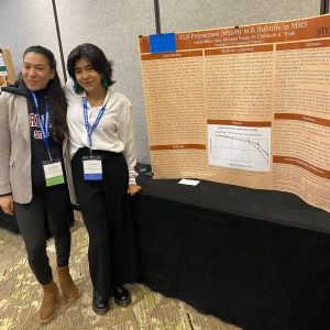 Two women stand next to a research poster propped up on a table.