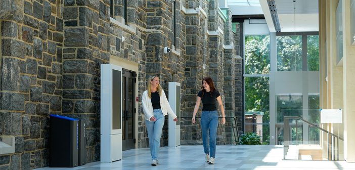 Two students walking together alongside the outside of hte gym