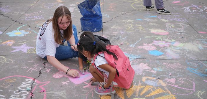 A student chalks the sidewalk with a child at Fordham Plaza