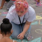 A student chalks the sidewalk with a child at Fordham Plaza