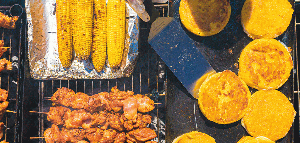 A grill, filled with corn, chicken and yellow patties..