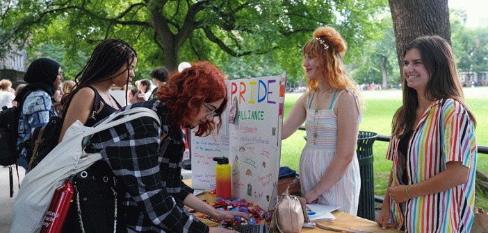 Pride Club table. Two female presenting on one side of the table, one student looking down at table.