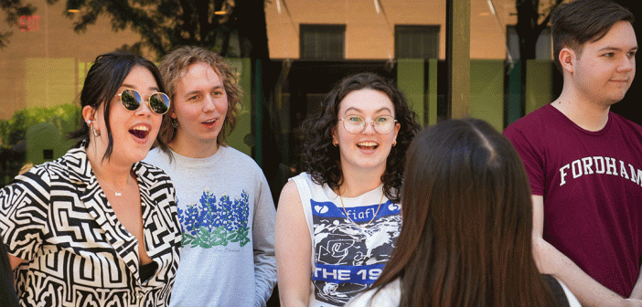 Two female presenting students and one male presenting student, in conversation smiling with another student.