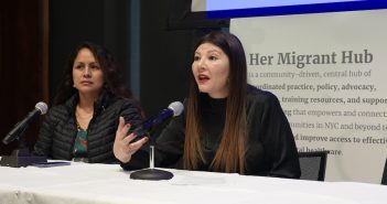 A student and a woman asylum seeker sit at a table and speak to an audience.