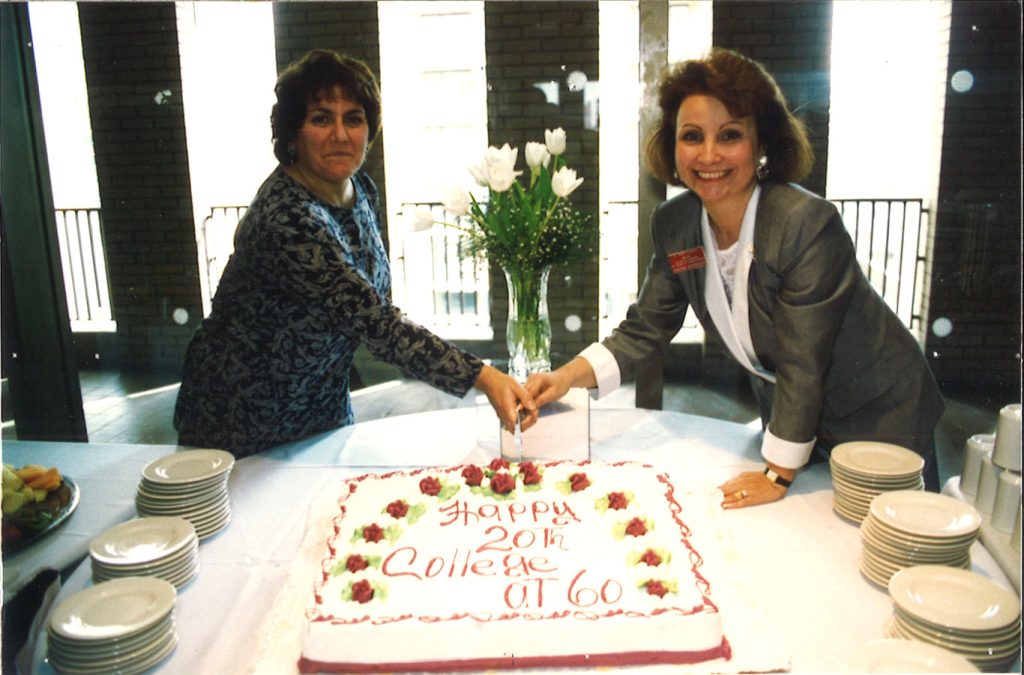 Two women cutting a cake together with a knife.