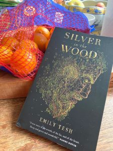 The book Silver in the Wood by Emily Tesh, down by a bag of oranges