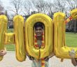 Three students hold jumbo gold balloons that spell out "HOLI."